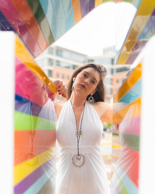 Woman in a white dress standing in front of a colorful, abstract sculpture.