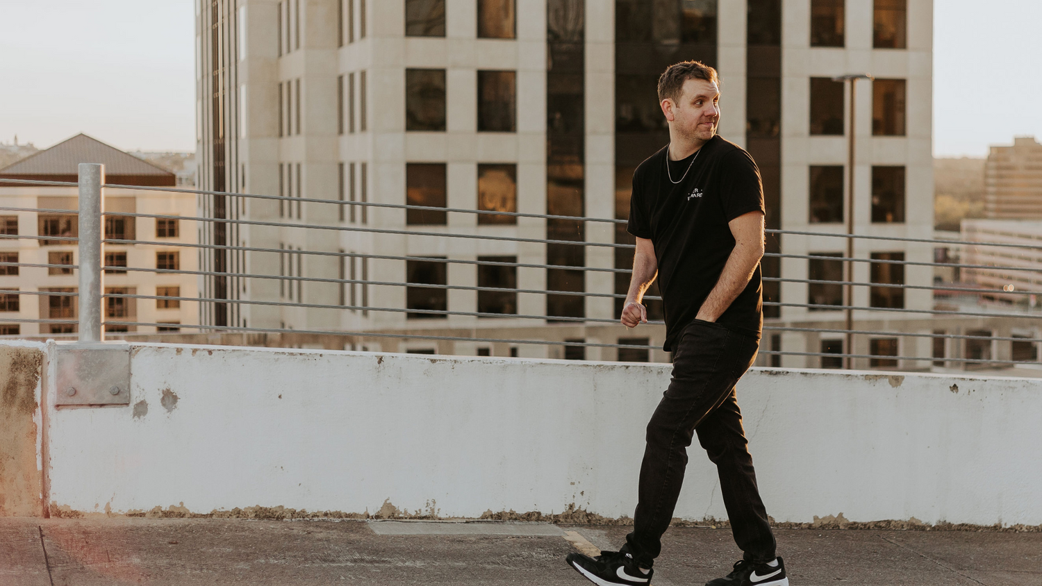 Colby walking on a rooftop with cityscape in the background