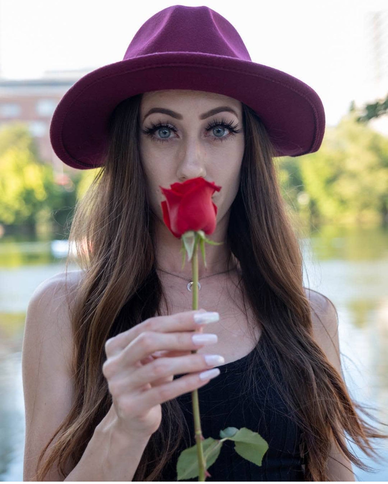 Woman wearing a purple hat holding a red rose near her face outdoors.