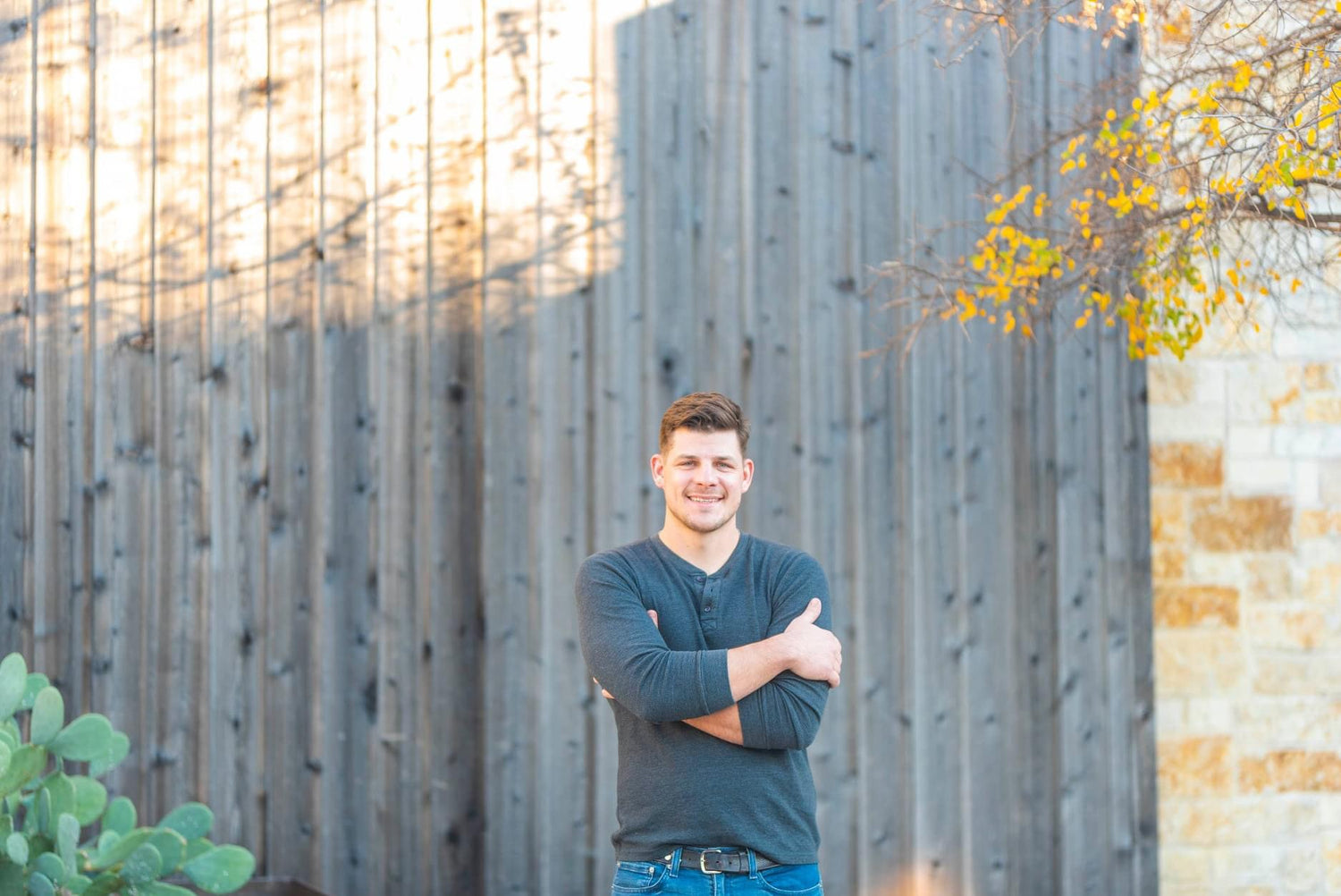 Man standing outdoors with a wooden fence and tree in the background