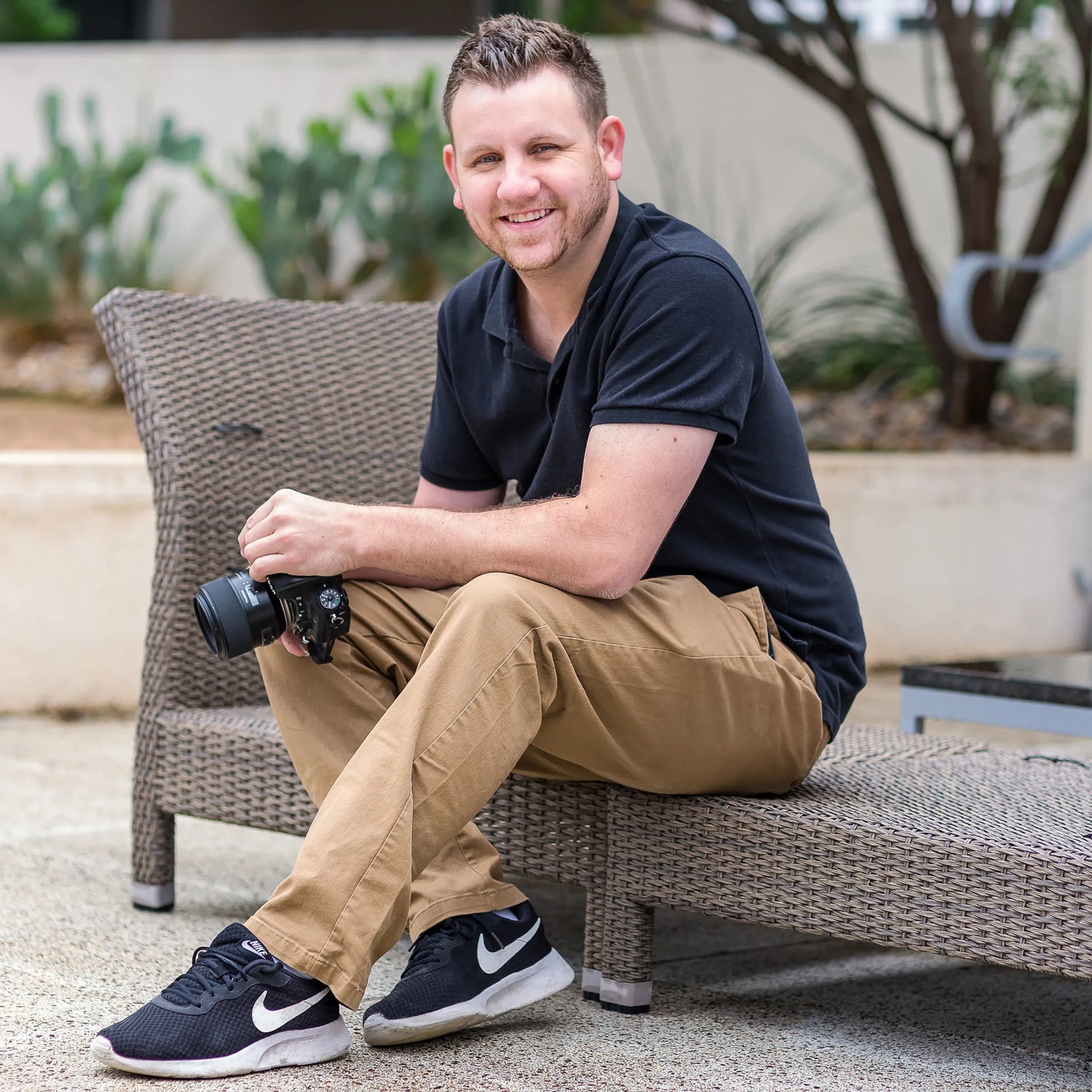 Man sitting on a wicker chair holding a camera outdoors